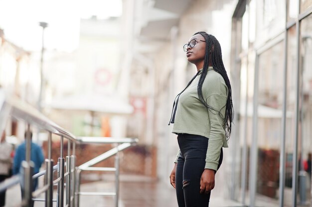 City portrait of positive young dark skinned female wearing green hoody and eyeglasses