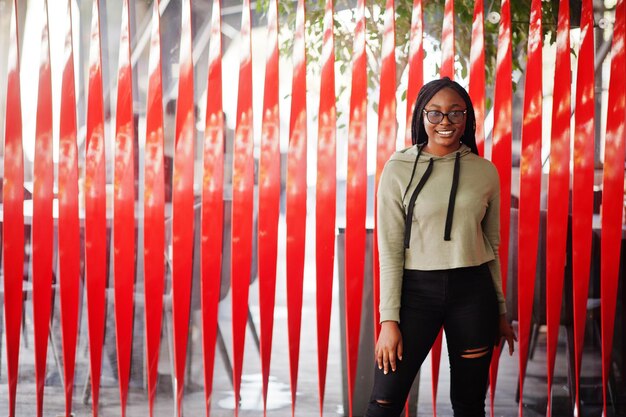 City portrait of positive young dark skinned female wearing green hoody and eyeglasses