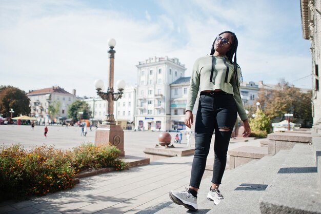 City portrait of positive young dark skinned female wearing green hoody and eyeglasses