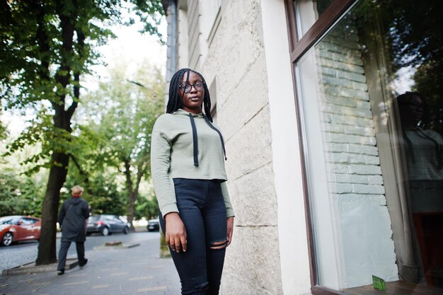 City portrait of positive young dark skinned female wearing green hoody and eyeglasses