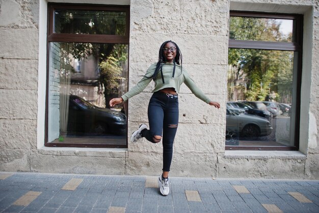 City portrait of positive young dark skinned female wearing green hoody and eyeglasses