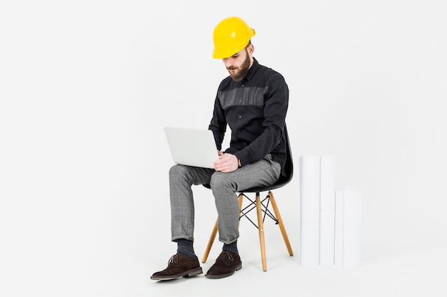 Foto gratuita ingegnere civile che indossa l'elmetto protettivo giallo facendo uso del computer portatile
