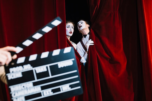 Clapperboard in front of mime couple standing behind the red curtain
