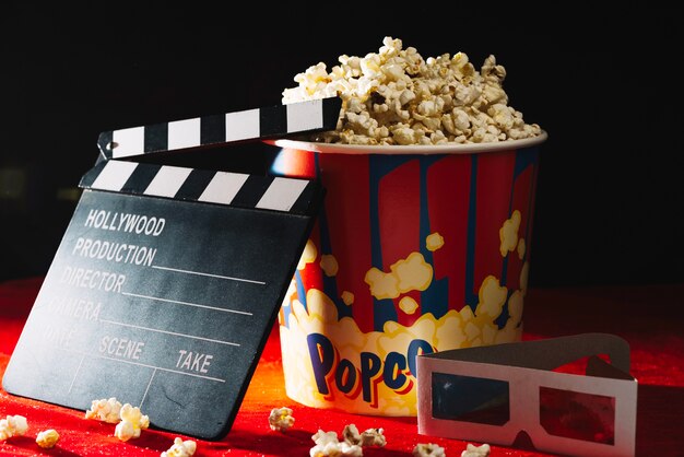 Clapperboard near popcorn bucket and 3D glasses