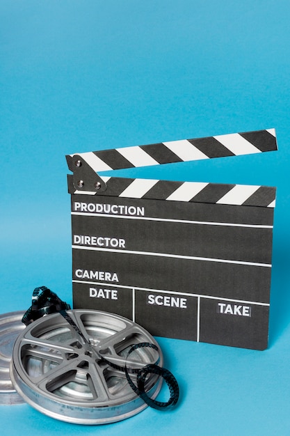 Clapperboard with film reel and film stripes against blue backdrop