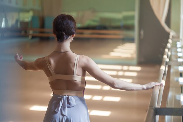 Classic ballet dancer posing at barre on rehearsal room