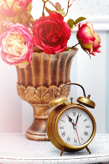 赤い花の背後にある明るいカラフルなレトロなインテリアの古典的な時計時計