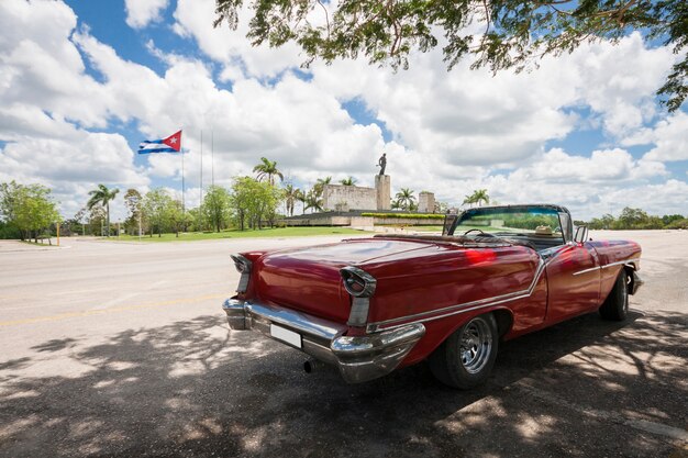 Classic convertible car with monument and cuban flag in background