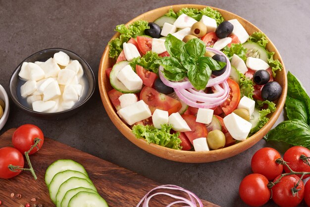 Классический греческий салат из свежих овощей, огурцов, помидоров, сладкого перца, листьев салата, красного лука, сыра фета и оливок с оливковым маслом. Здоровая еда, вид сверху