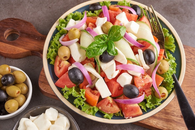 Classic greek salad of fresh vegetables, cucumber, tomato, sweet pepper, lettuce, red onion, feta cheese and olives with olive oil. Healthy food, top view