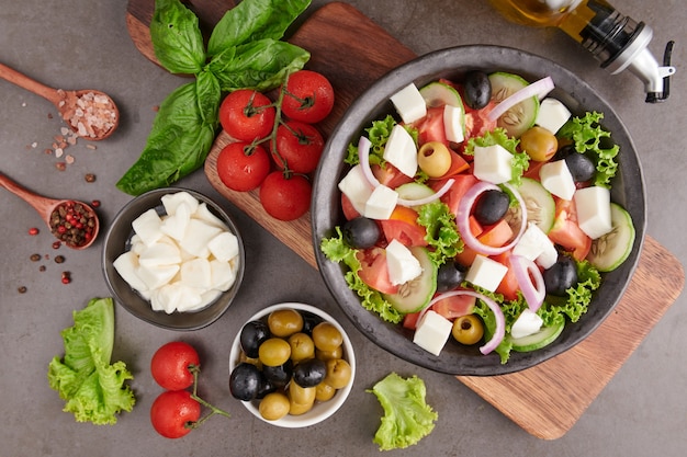 Классический греческий салат из свежих овощей, огурцов, помидоров, сладкого перца, листьев салата, красного лука, сыра фета и оливок с оливковым маслом. Здоровая еда, вид сверху