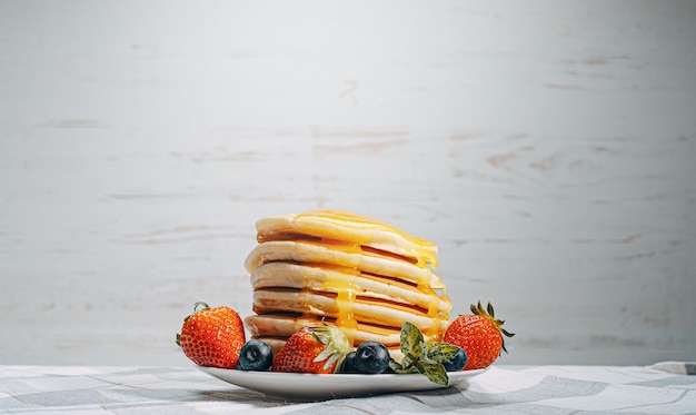 On classic homemade pancakes with berries on a white saucer on a light wooden background in a rustic style