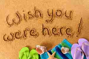 Free photo classic postcard message written on a sandy beach, with beach towel, starfish and flip flops