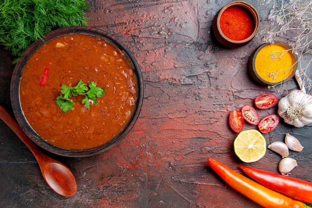 Классический томатный суп в коричневой миске и разные специи, чеснок, лимон на столе смешанных цветов