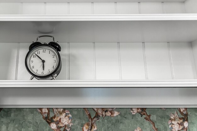Free Photo classic vintage alarm clock on an empty white shelf in a room interior.