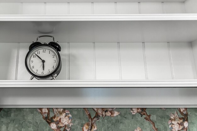 실내의 빈 흰색 선반에 있는 고전적인 빈티지 알람 시계.