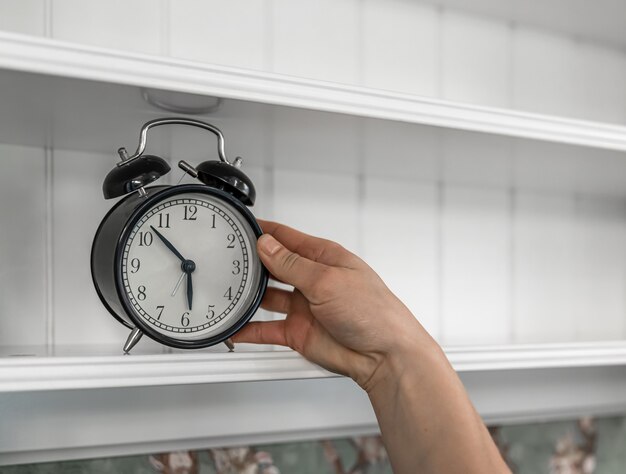 Classic vintage alarm clock on an empty white shelf in a room interior.