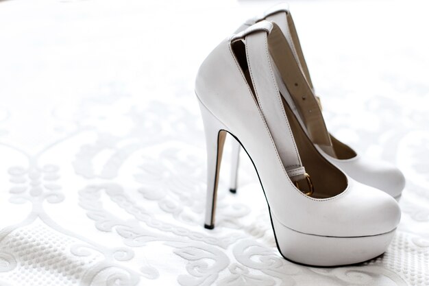 上品な白いプラットフォームの靴は、白い刺繍布に立つ