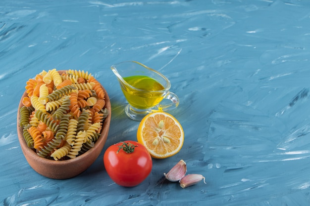 A clay board of raw pasta with oil and fresh red tomatoes on a blue background. 