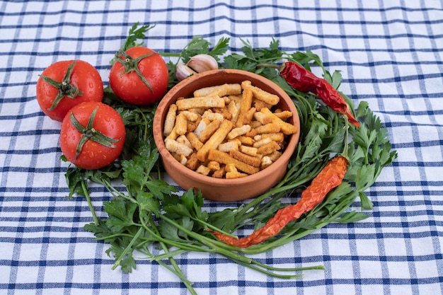 A clay bowl of breadsticks with vegetables on a tablecloth