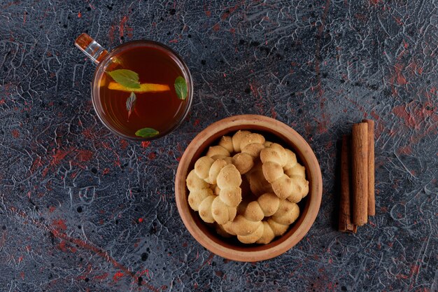 A clay bowl of cupcakes round with a hole and a glass cup of hot tea 