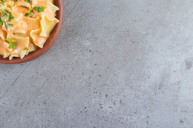 Clay bowl of delicious creamy macaroni on stone background. 