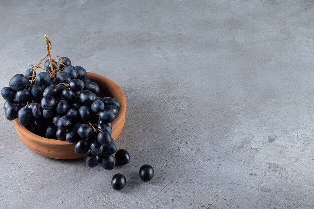 Clay bowl of fresh black grapes on stone table.