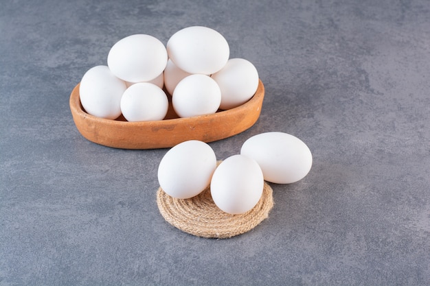 Clay bowl full of raw white eggs on stone table.