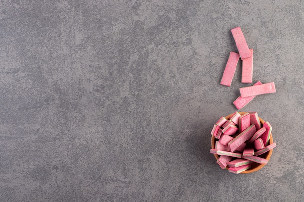 Clay bowl of long pink chewy sticks on stone table.