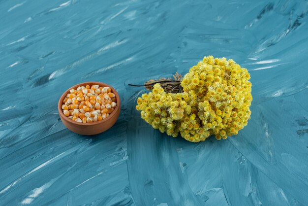 Clay bowl of raw corn kernels on blue surface.