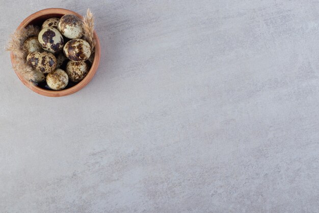 Clay bowl of raw quail eggs on stone table.