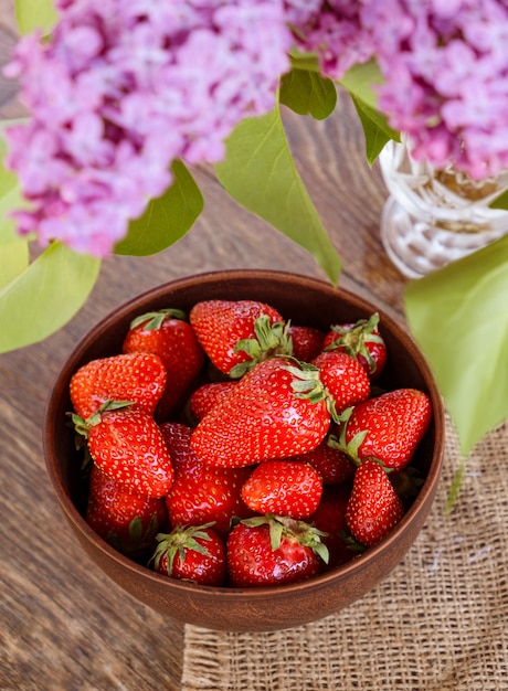 Clay bowl with red strawberry on wooden table.