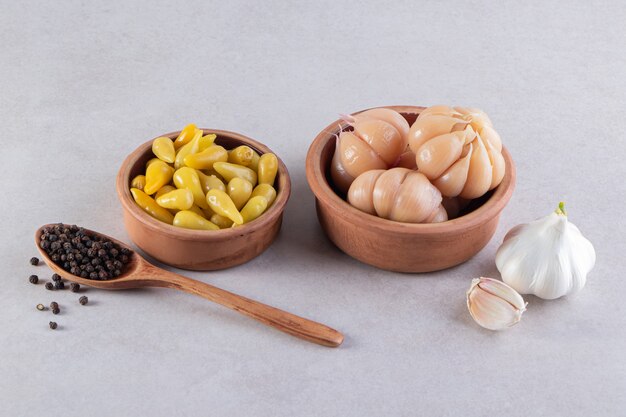 Clay bowls of pickled garlic and chili peppers on stone table.