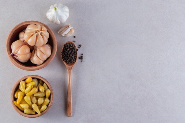 Clay bowls of pickled garlic and chili peppers on stone table.