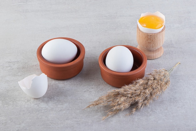 Clay bowls of white raw eggs with egg yolk on stone table.