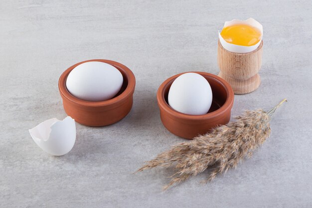 石のテーブルに卵黄と白い生卵の粘土ボウル。
