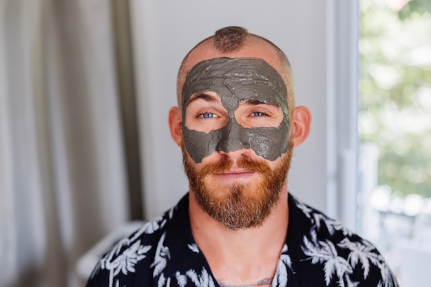 clay mask on young handsome mans face in beauty clinic