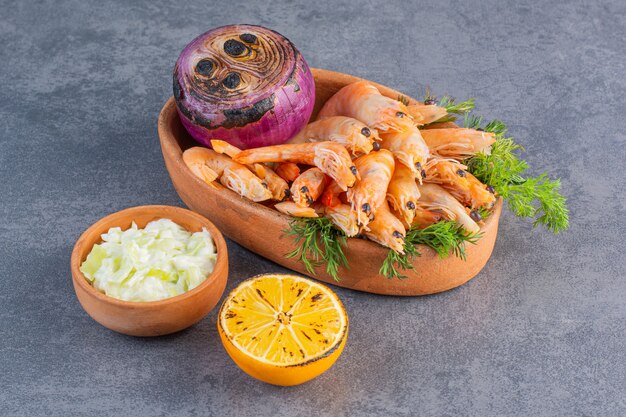 A clay plate of delicious shrimps with sliced lemon and onion on a stone surface 