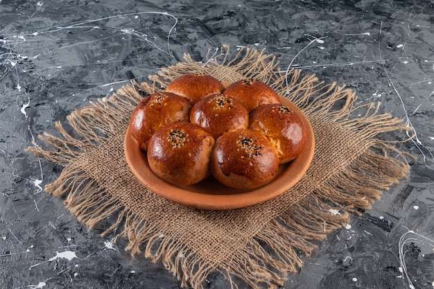 Clay plate of fresh pastry with sesame seeds on marble table.