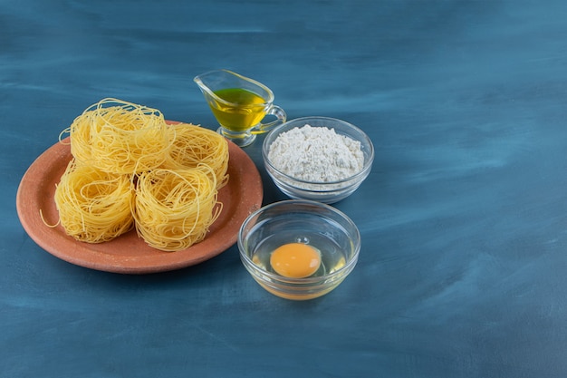 A clay plate of raw dry nest pasta on a dark-blue background .