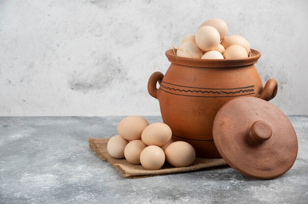 Clay pot full of raw chicken eggs on marble.