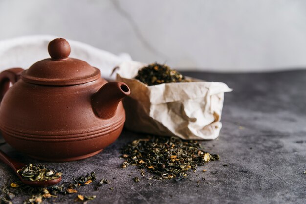 Clay teapot and dried leaves on concrete