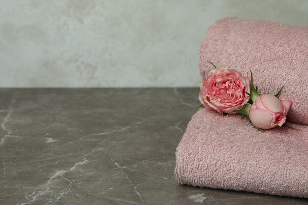 Чистые розовые сложенные полотенца и розы на сером текстурированном столе
