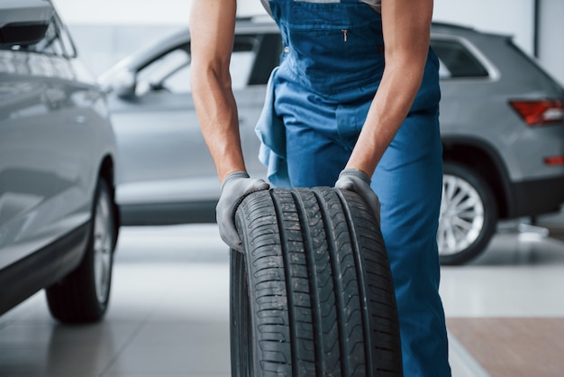 Clean room. Mechanic holding a tire at the repair garage. Replacement of winter and summer tires