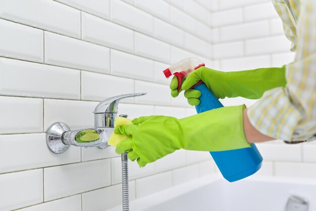 Cleaning the bathroom, a woman washing a tile wall and a mixer with a washcloth with detergent