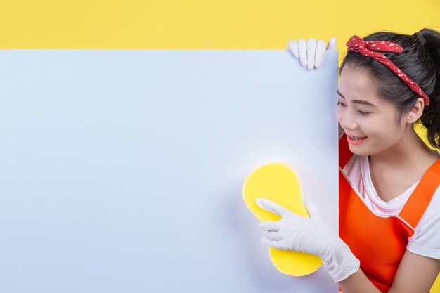 クリーニング。美しい女性は広告メッセージを出すためにホワイトボードを持ち、黄色の上に清掃用具を持ちます。