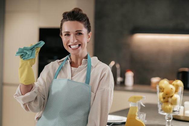 Уборка кухни. Улыбающаяся молодая домохозяйка держит в руках дезинфицирующий спрей