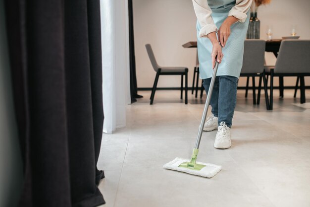 Cleaning the kitchen. A young woman in apron cleaning the floor in the kitchen