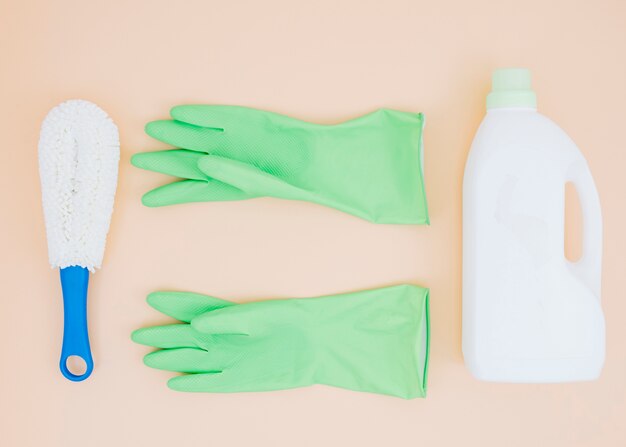 Cleaning supplies like brush; green gloves and detergent can on peach backdrop