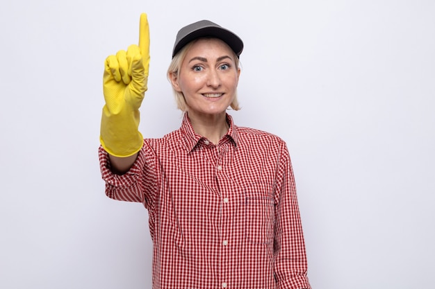 Foto gratuita donna delle pulizie in camicia a quadri e berretto con guanti di gomma che sembrano sorridenti e mostrano il dito indice